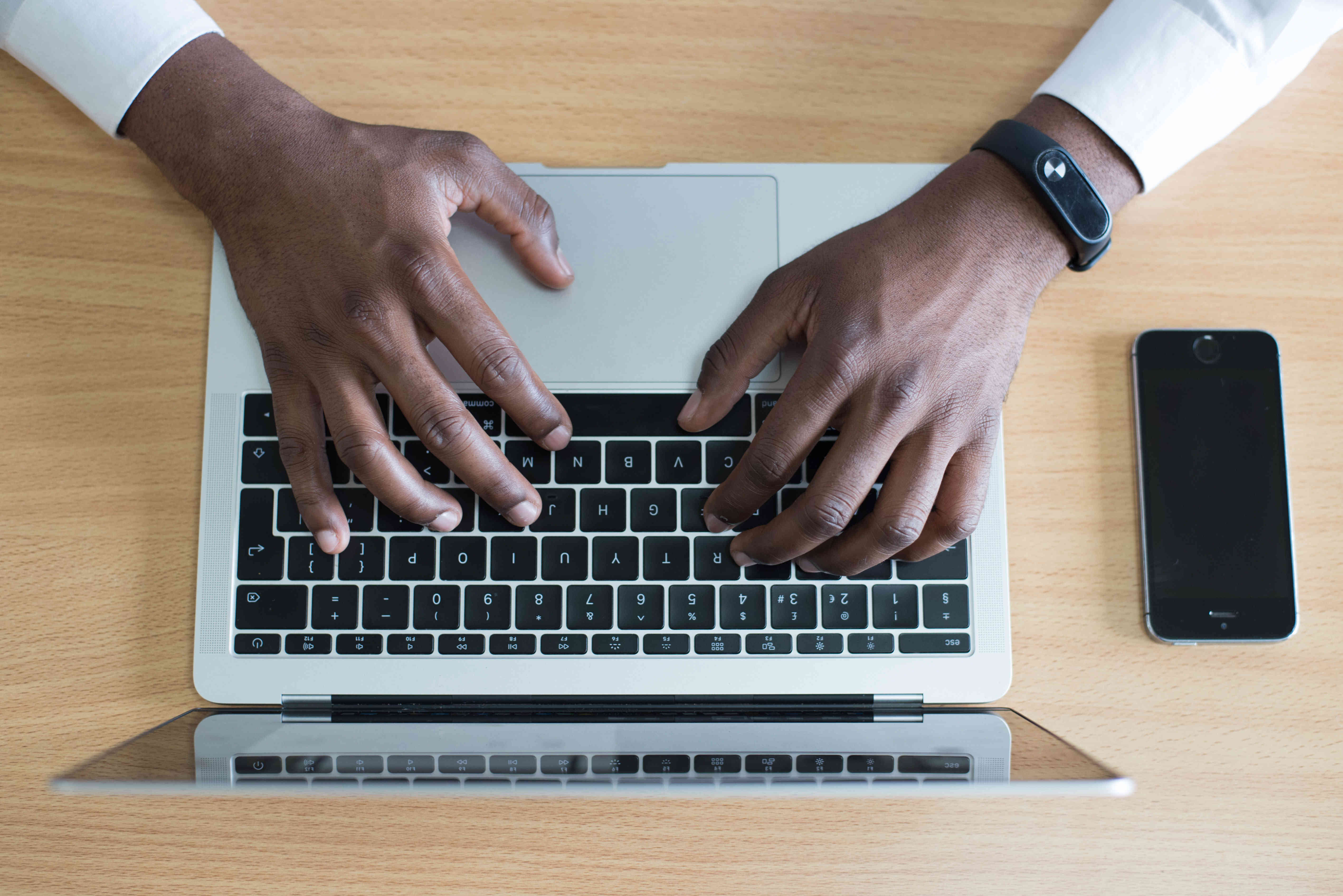 Hands typing on a laptop with a cellphone next to it